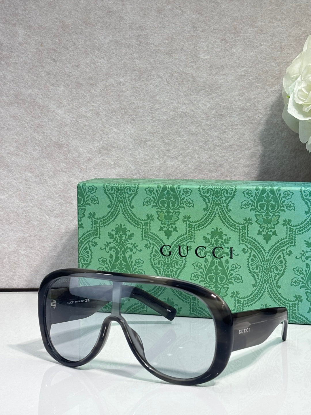 Gucci oversized glasses with black frame and dark lenses, beside green logo case