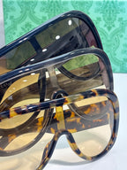 Gucci sunglasses close-up: oval tinted lenses, dark navy frame with tortoiseshell accents