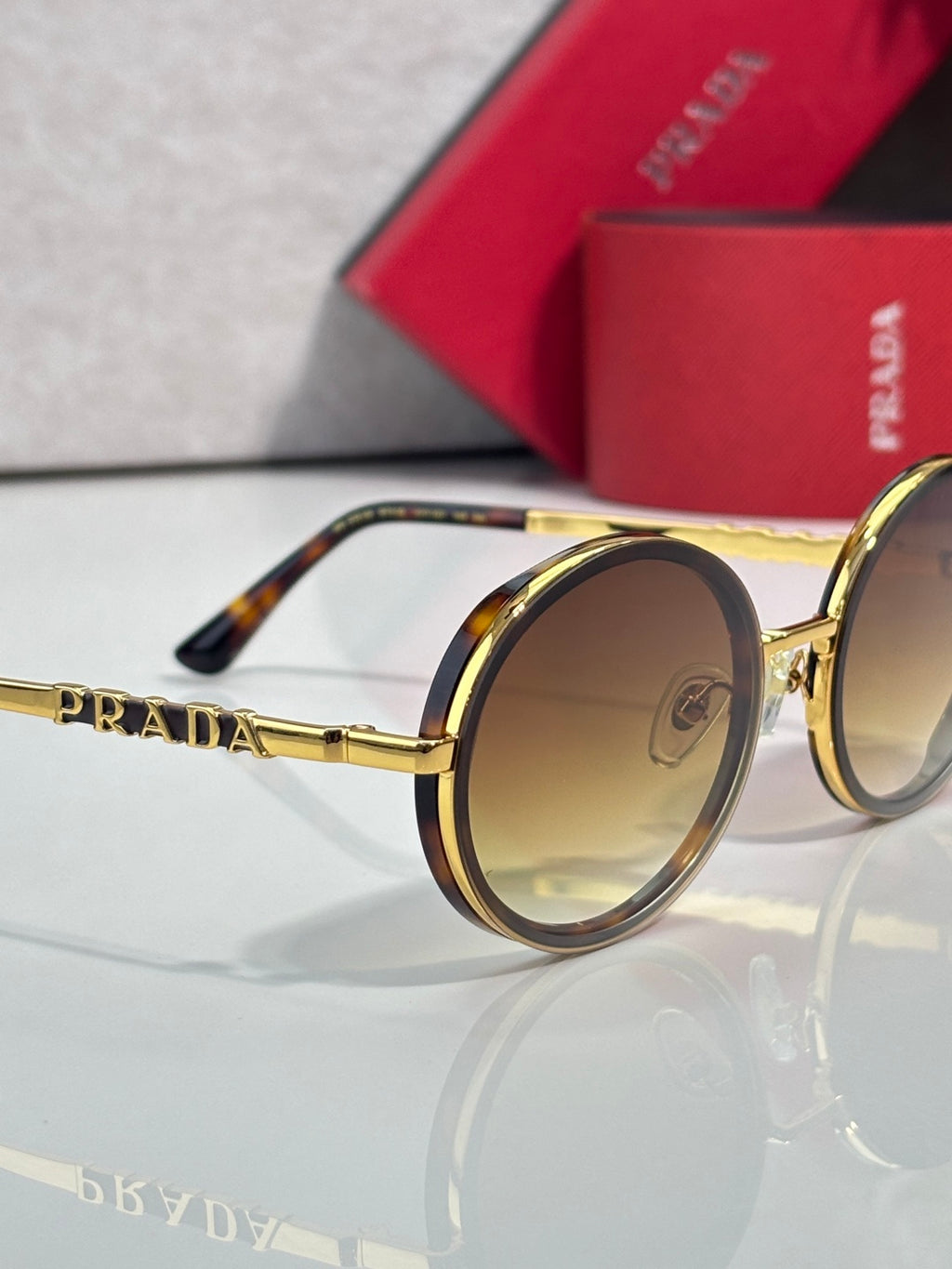 Prada round sunglasses close-up with gold-tone frame and amber-tinted lenses, tortoise tips