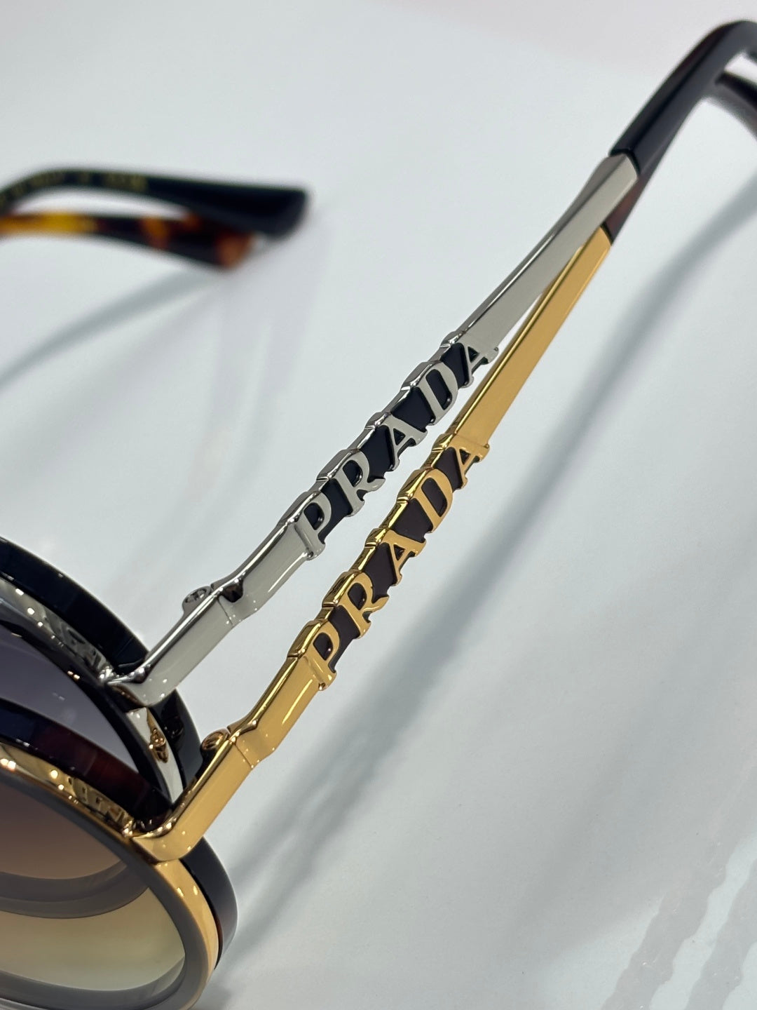 Prada sunglasses temple close-up with gold-tone bar and Prada lettering, dark lens