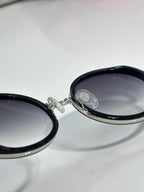 Prada round eyeglasses hinge close-up, dark lens with silver frame detail