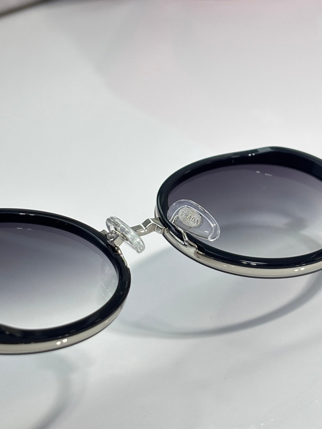 Prada round eyeglasses hinge close-up, dark lens with silver frame detail