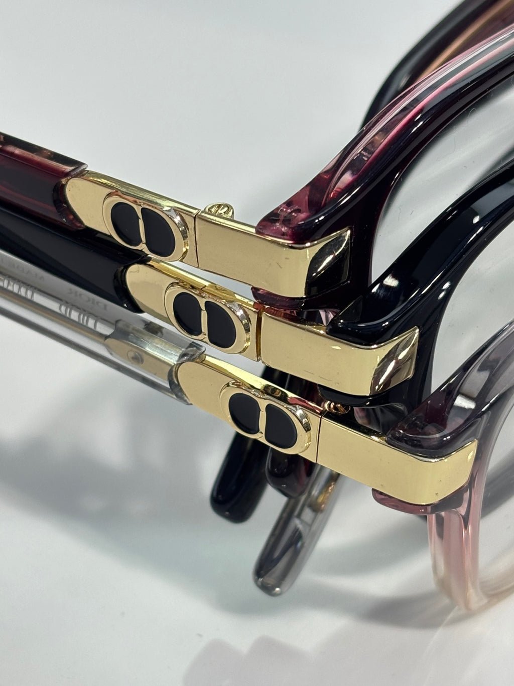Rectangular eyeglasses temple close-up with gold logo plates and dark marbled frame