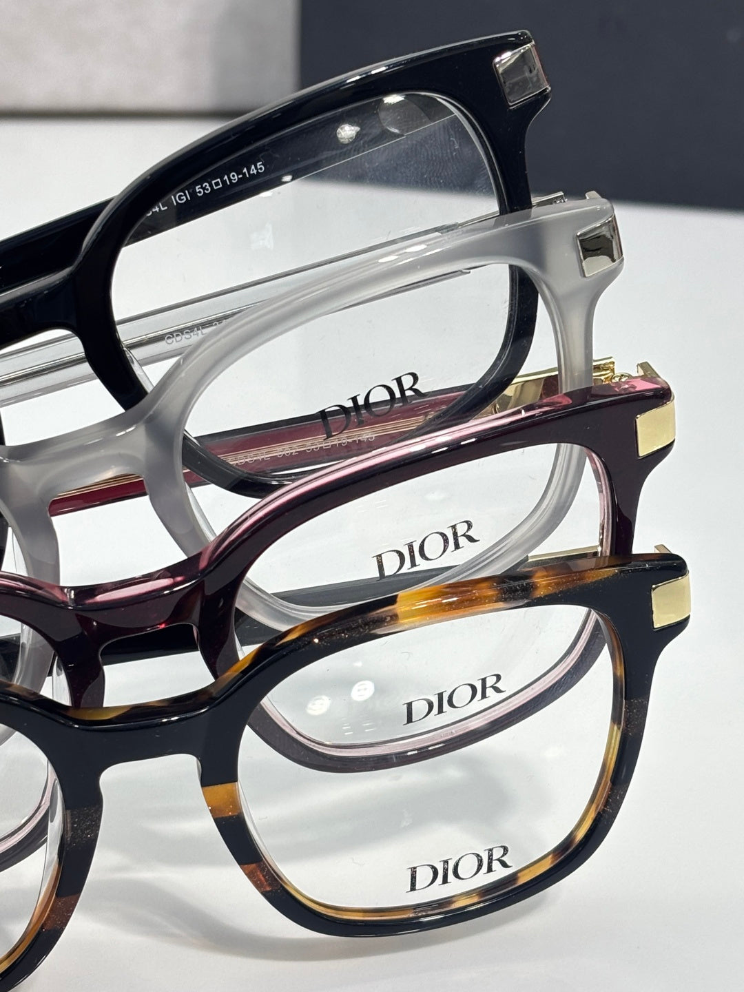 Close-up of Dior eyeglasses frames in black, white, and tortoiseshell with clear lenses