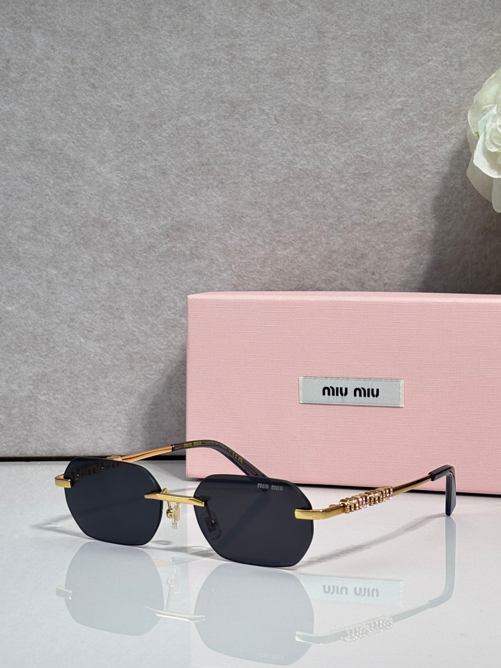 MiuMiu sunglasses with gold metal frame, dark lenses, and embellished temple bar