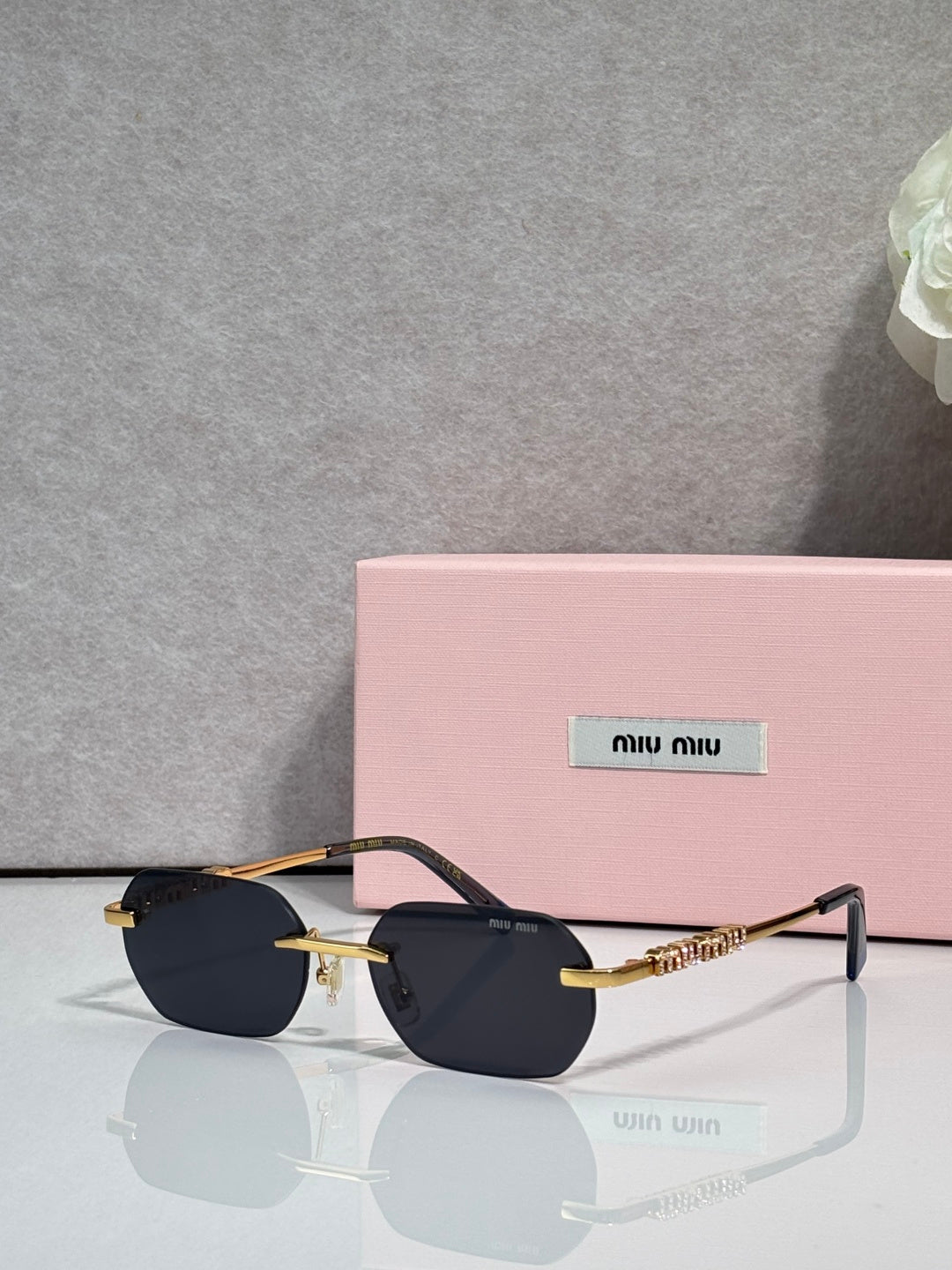 MiuMiu sunglasses with gold metal frame, dark lenses, and embellished temple bar