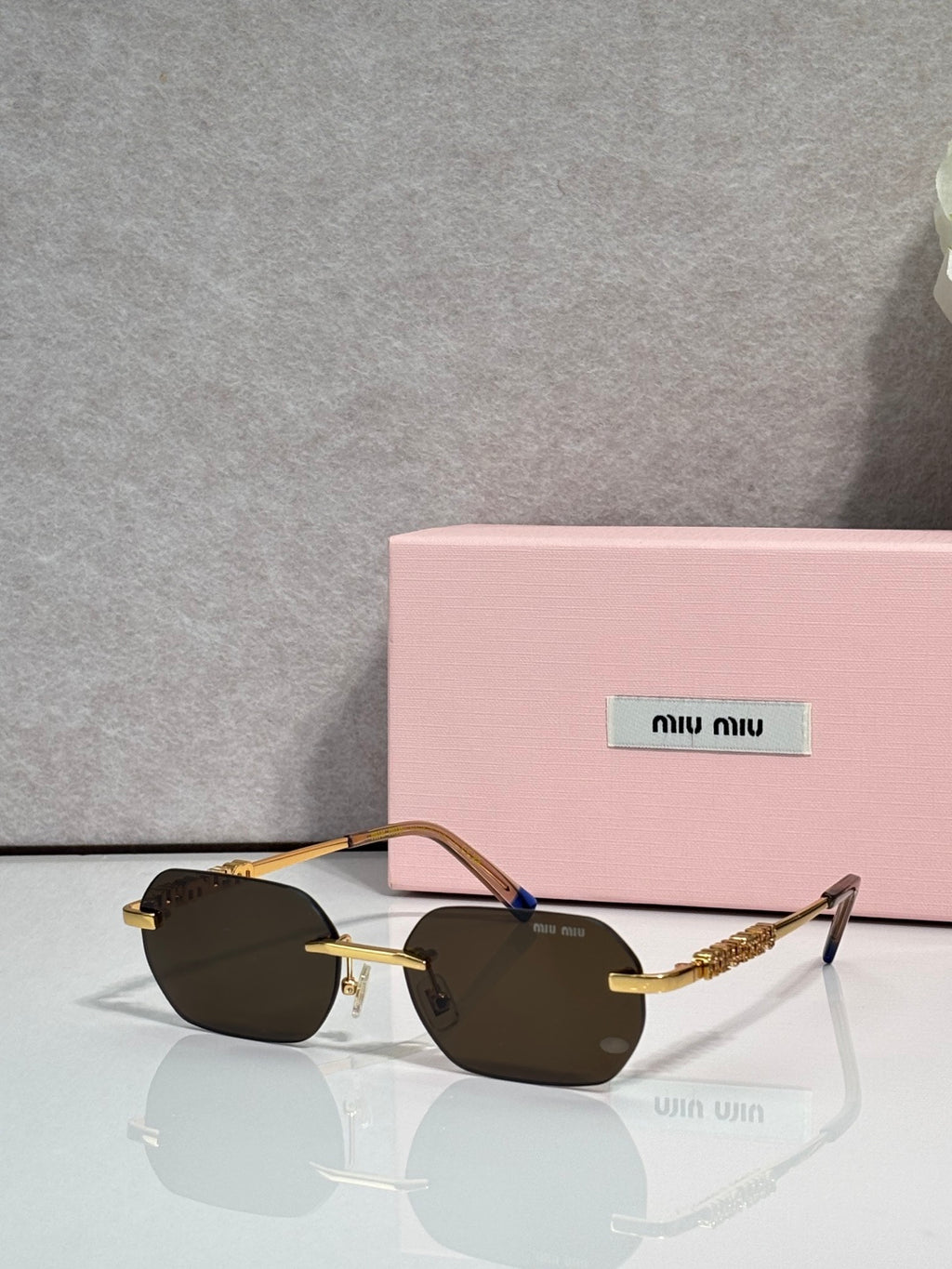 MiuMiu sunglasses with gold metal frame, dark lenses, and blue accent at temple