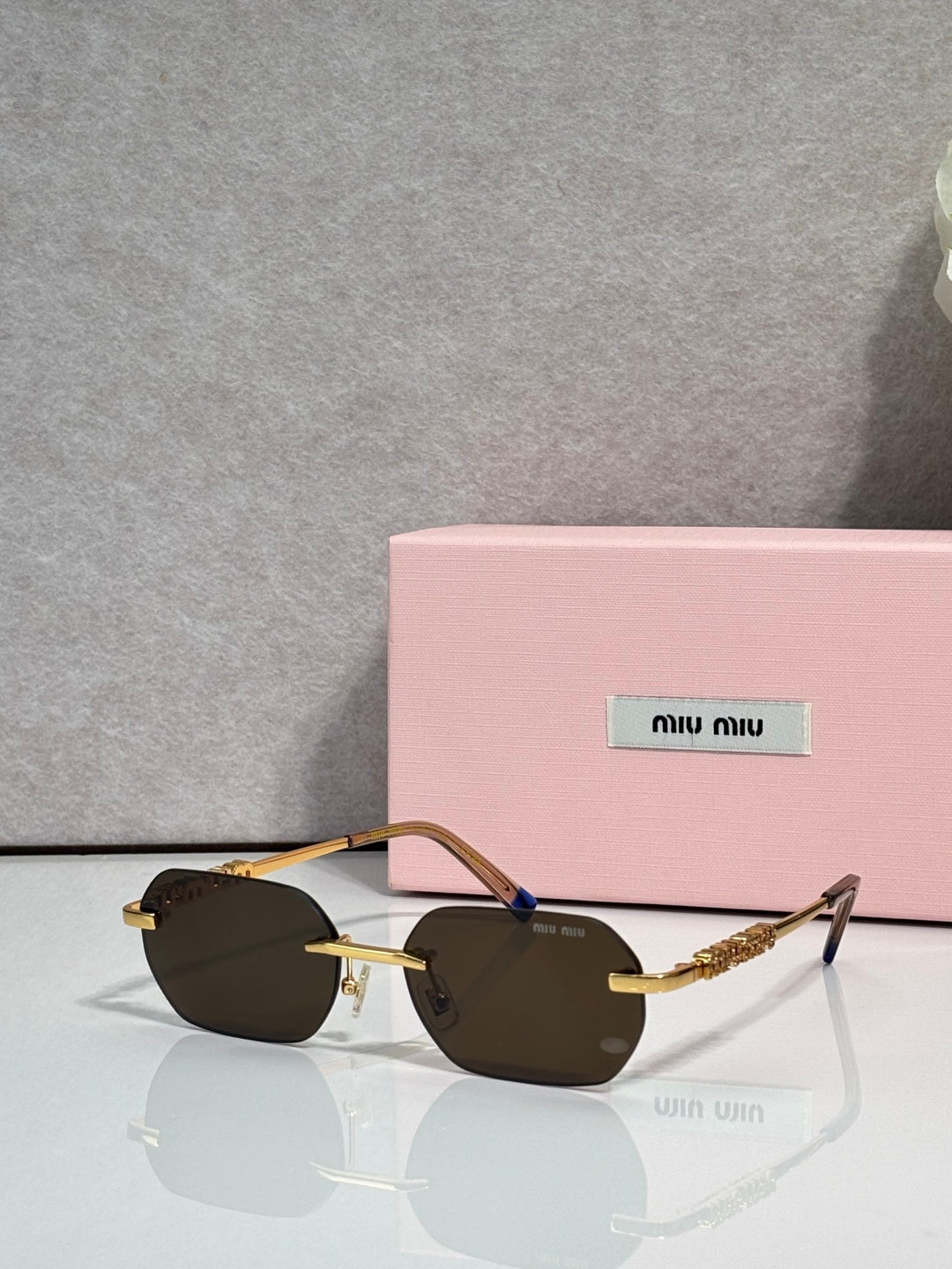 MiuMiu sunglasses with gold metal frame, dark lenses, and blue accent at temple