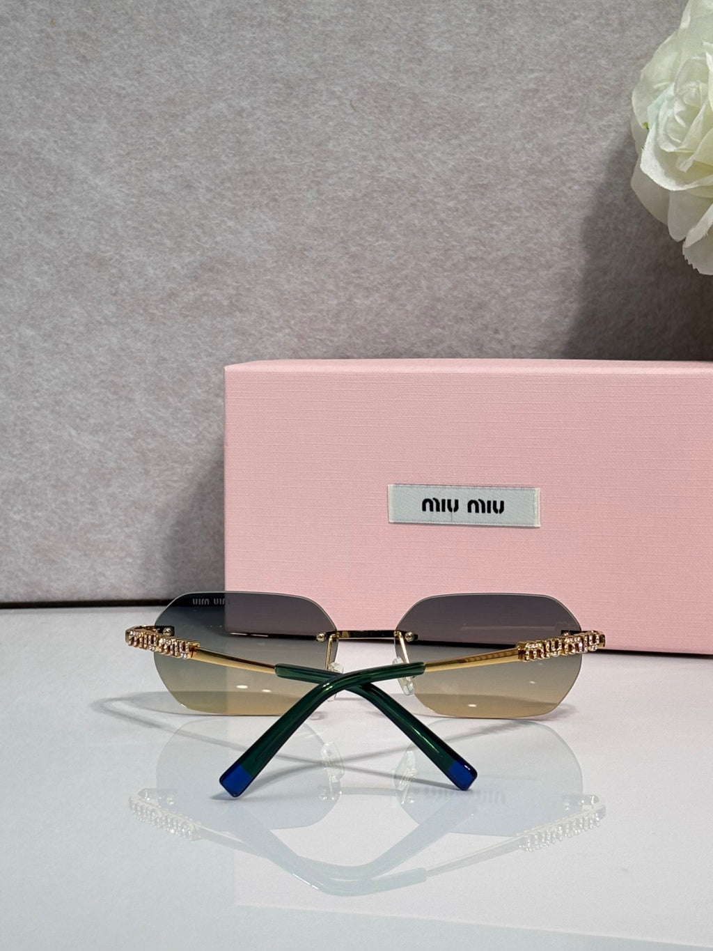 MiuMiu sunglasses with gold metal frame, dark lenses, and blue accent at temple