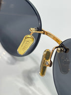 Gold-tone hinge detail on dark round sunglasses with black temple tips
