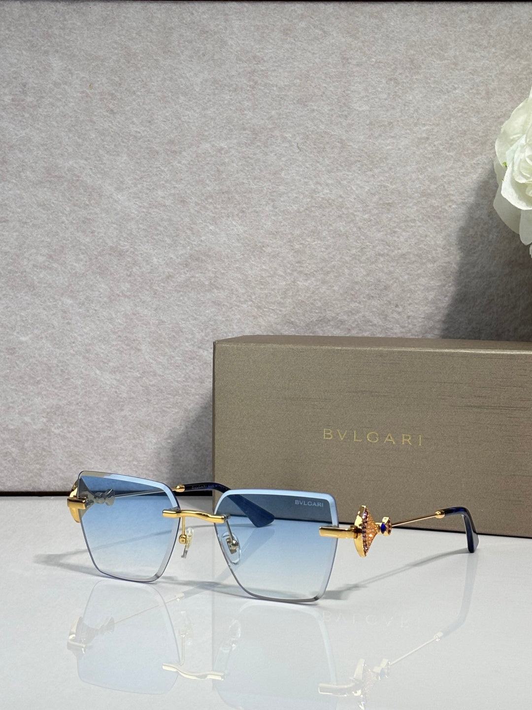 Gold-framed square sunglasses with light blue lenses and butterfly bridge charm