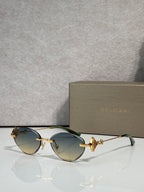 Sunglasses with green-tinted lenses and gold metal frame, jeweled bow accent