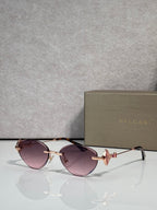 Sunglasses with purple-tinted lenses and gold metal frame, jeweled bow accent