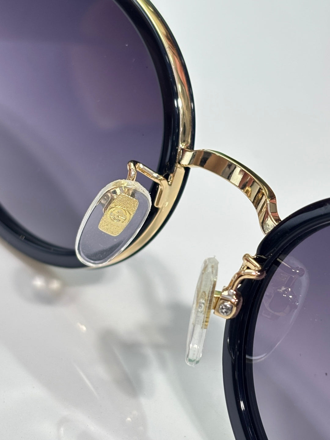 Gucci sunglasses close-up of round dark lens, gold hinge detail, and temple emblem