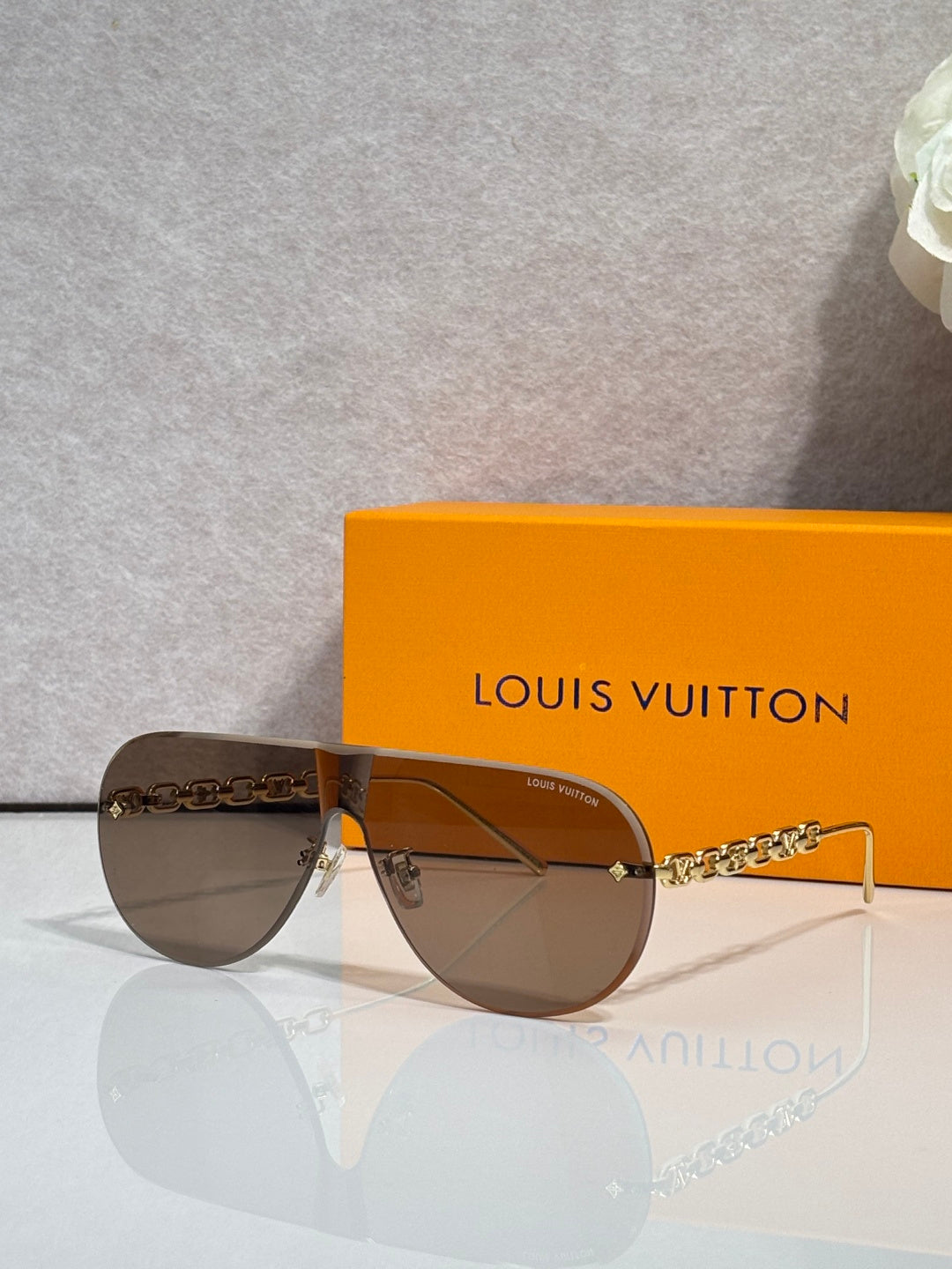 Sunglasses with dark brown lenses and gold chain temple, thin metal silhouette