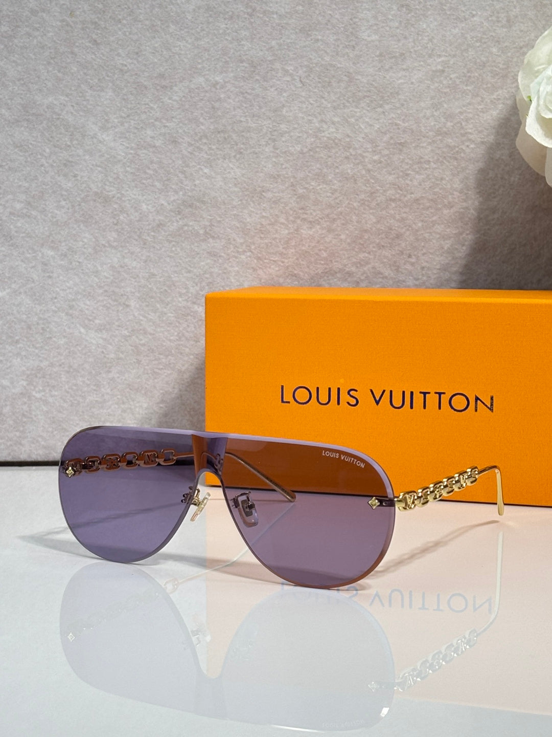 Sunglasses with purple-tinted lenses and gold-tone chain detail, thin metal frame
