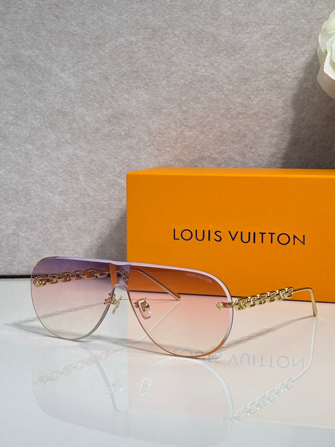 Sunglasses with clear-toned frame edges and gold chain temple, brown gradient lenses