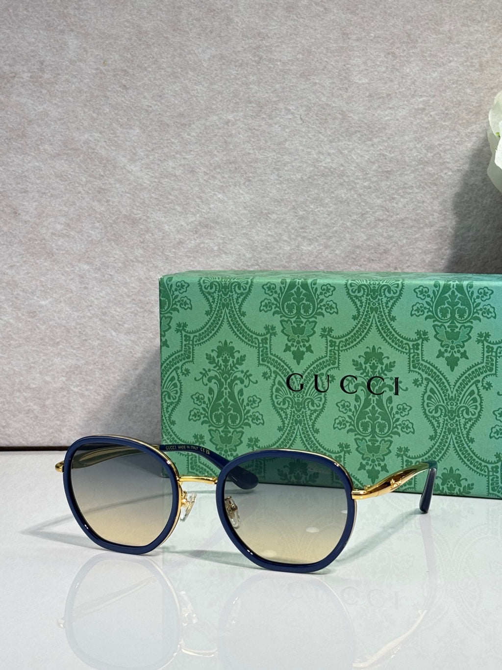 Round sunglasses with navy frames and gold-tone details, blue-tinted lenses.