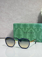 Round sunglasses with navy frames and gold-tone details, blue-tinted lenses.