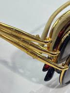 Sunglasses close-up of gold temple with engraved logo.