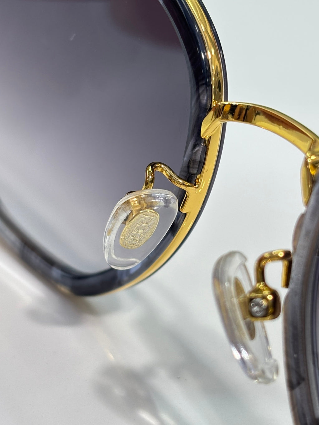 Sunglasses close-up of gold hinge and clear charm on temple.