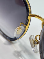 Sunglasses close-up of gold hinge and clear charm on temple.