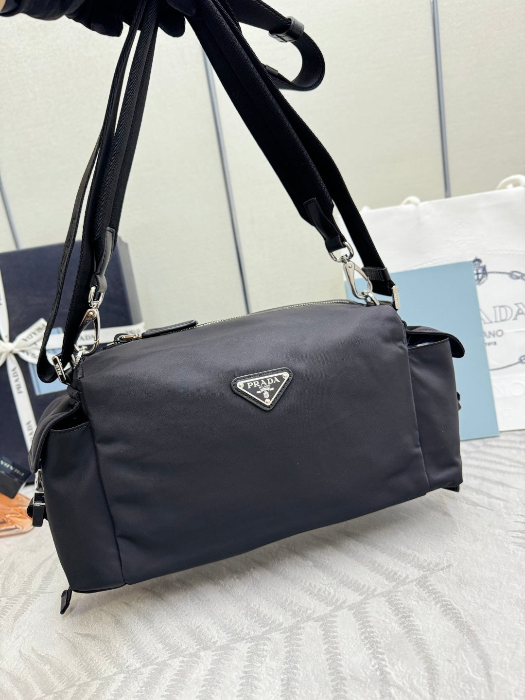 Prada dark nylon handbag with top handles and shoulder strap, angled side view with logo.