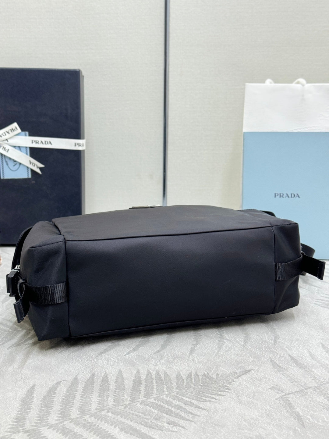 Prada dark nylon handbag with structured back panel and shoulder strap, side view.