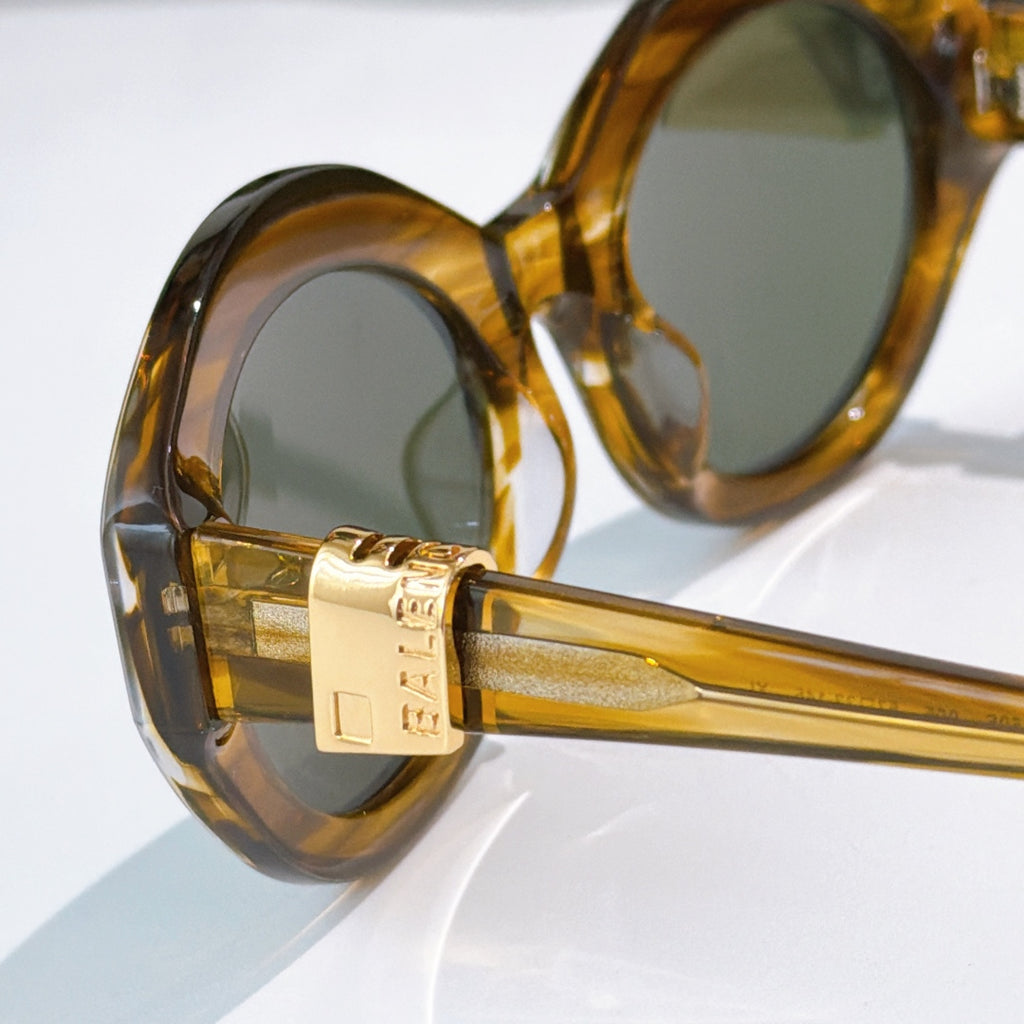 Close-up of amber round sunglasses with green tinted lenses and gold logo hinge