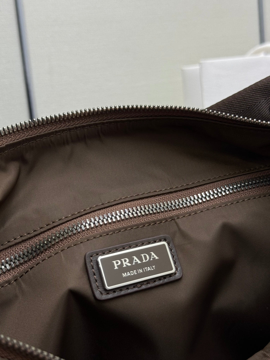 Interior view of brown nylon bag with PRADA leather logo patch near zipper