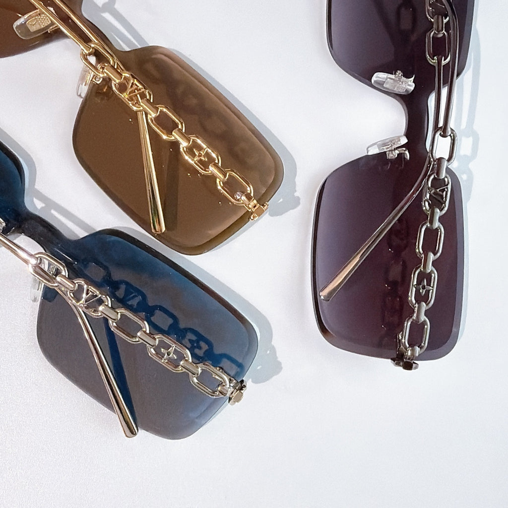 Multiple sunglasses with tinted lenses and chain temple details in brown, blue, and purple