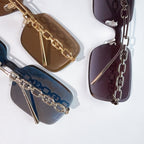 Multiple sunglasses with tinted lenses and chain temple details in brown, blue, and purple