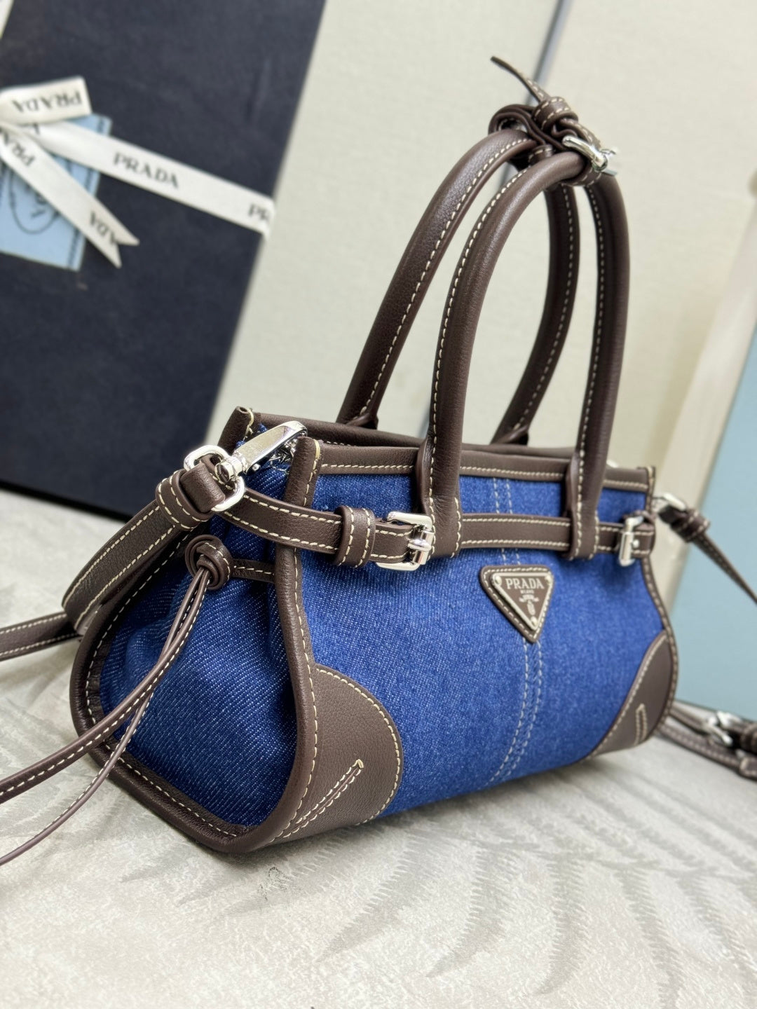 Blue denim Prada handbag side view with brown leather handles and logo triangle