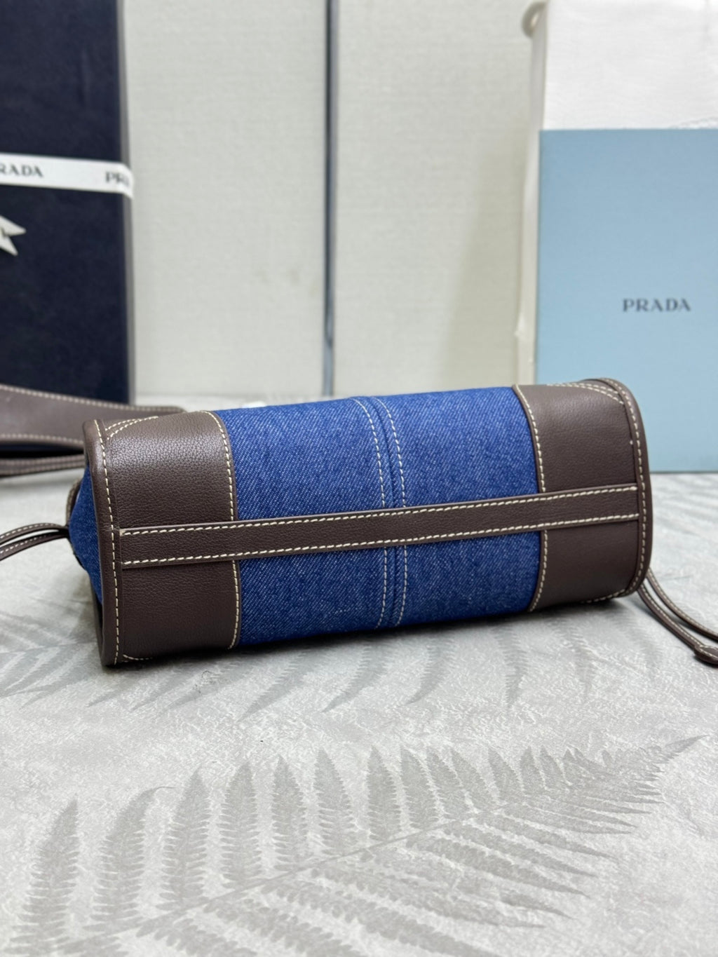 Cylindrical blue denim Prada bag with brown leather strap handles and zip closure