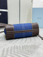 Cylindrical blue denim Prada bag with brown leather strap handles and zip closure