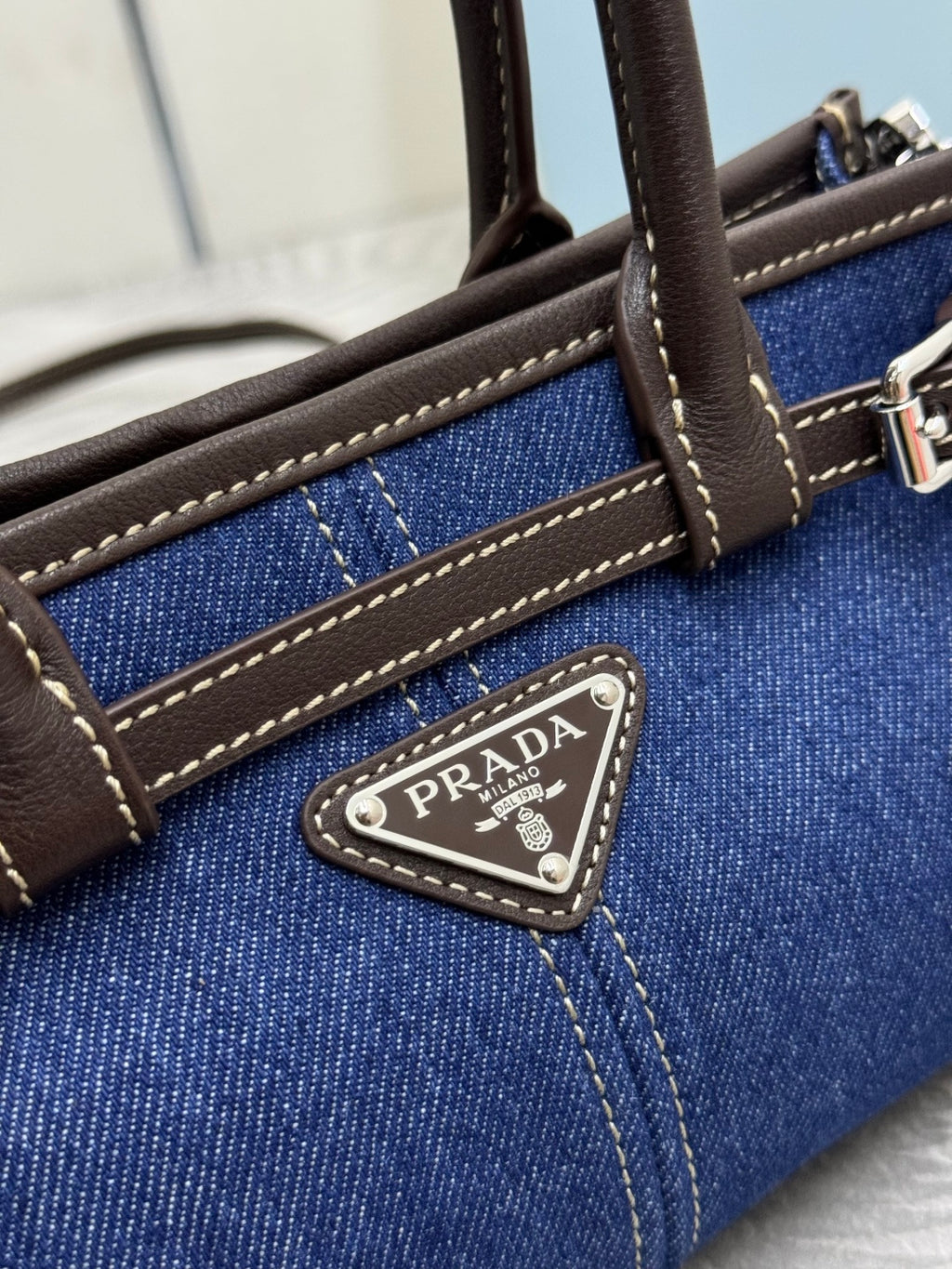 Close-up of blue denim Prada handbag with brown leather strap and logo plaque
