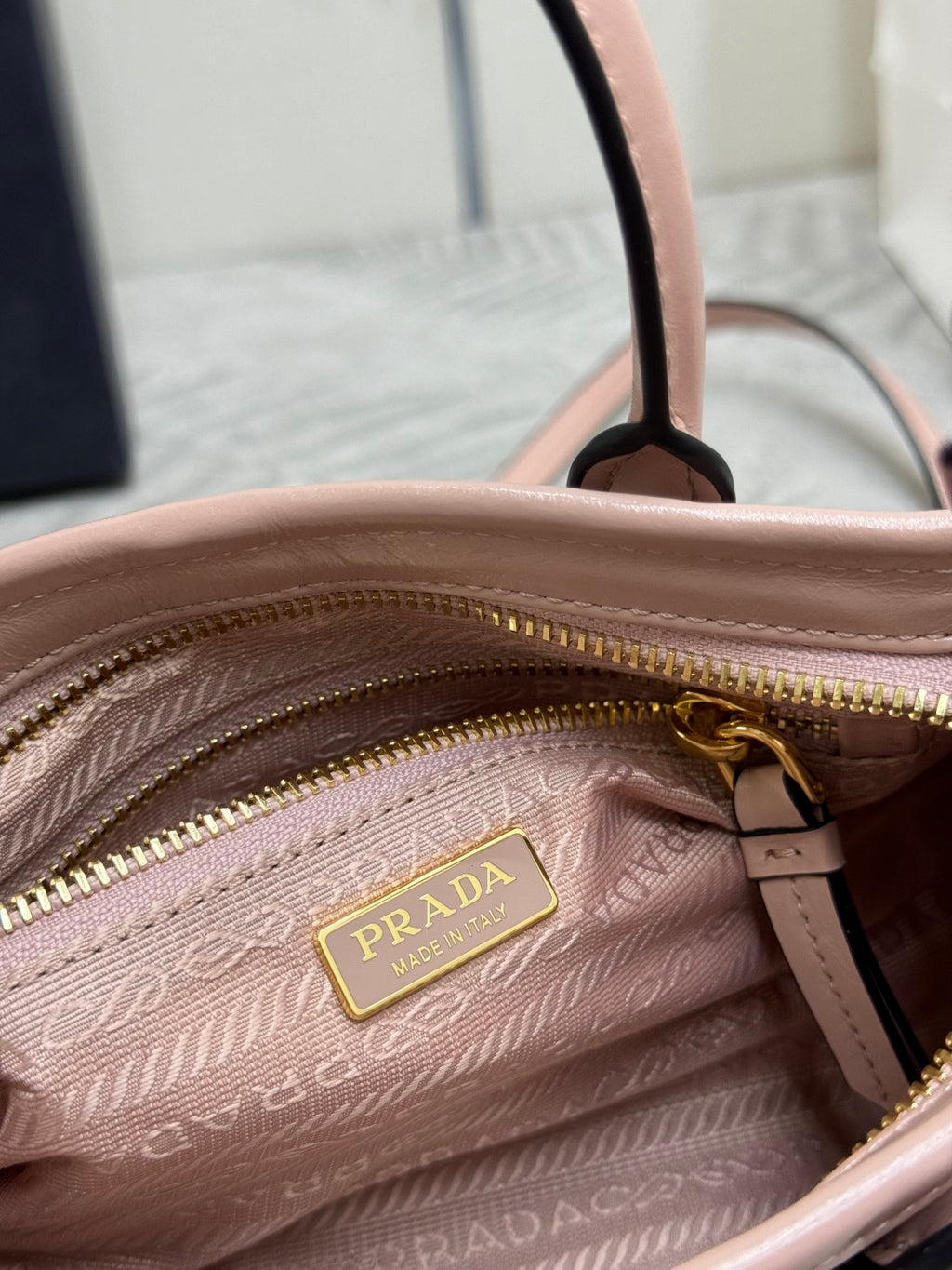 Prada light pink mini bag close-up of gold logo zipper pull and textured lining