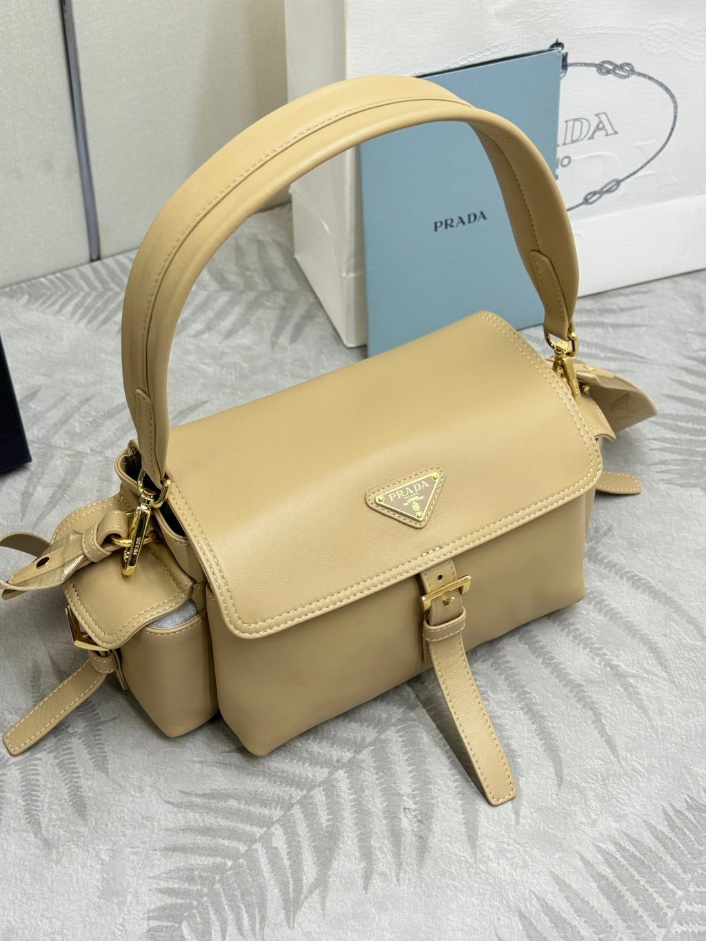 Beige leather shoulder bag with flap closure and triangular logo plate on front