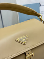 Beige leather bag with triangular PRADA logo plaque and gold clasp at strap