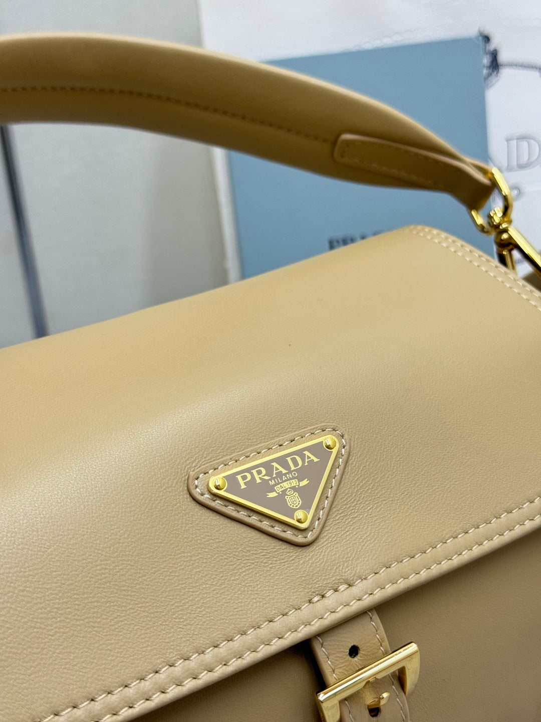 Beige leather bag with triangular PRADA logo plaque and gold clasp at strap