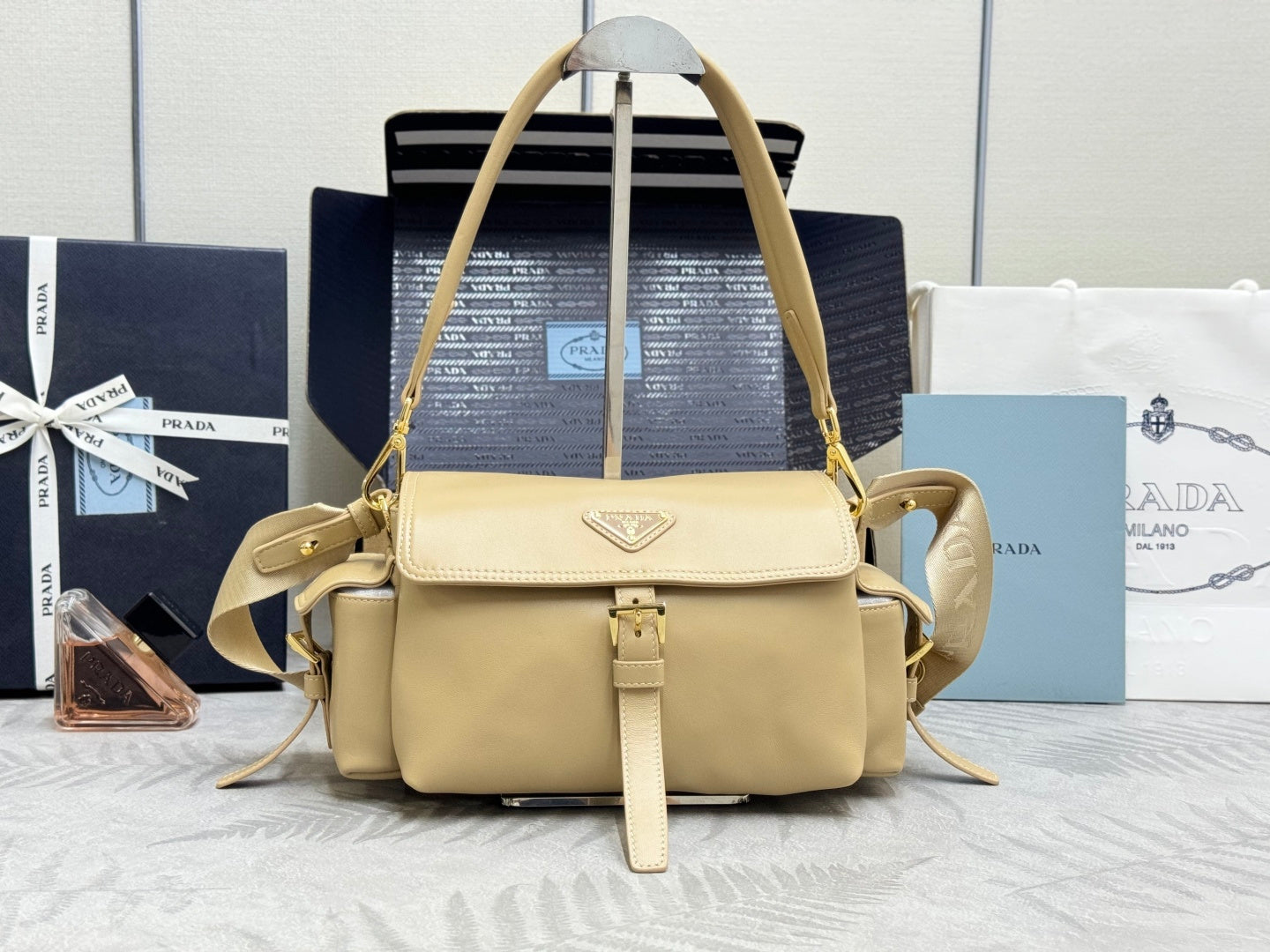 Beige leather shoulder bag with top handle, flap front, gold hardware, and logo plaque