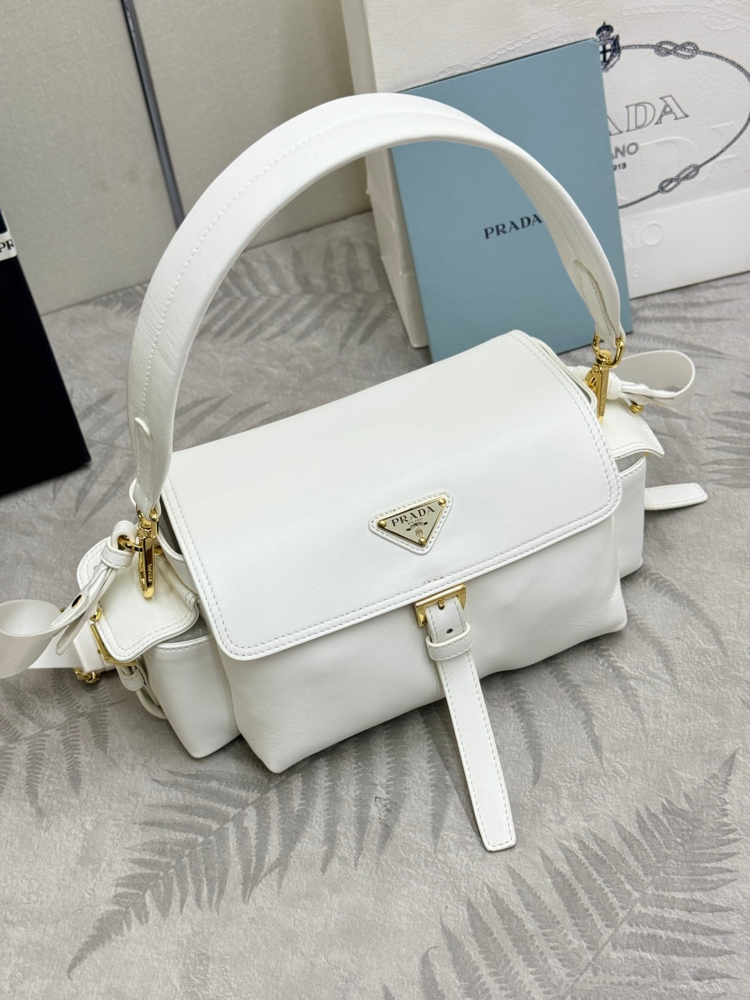 White Prada handbag with adjustable strap and gold logo emblem on front
