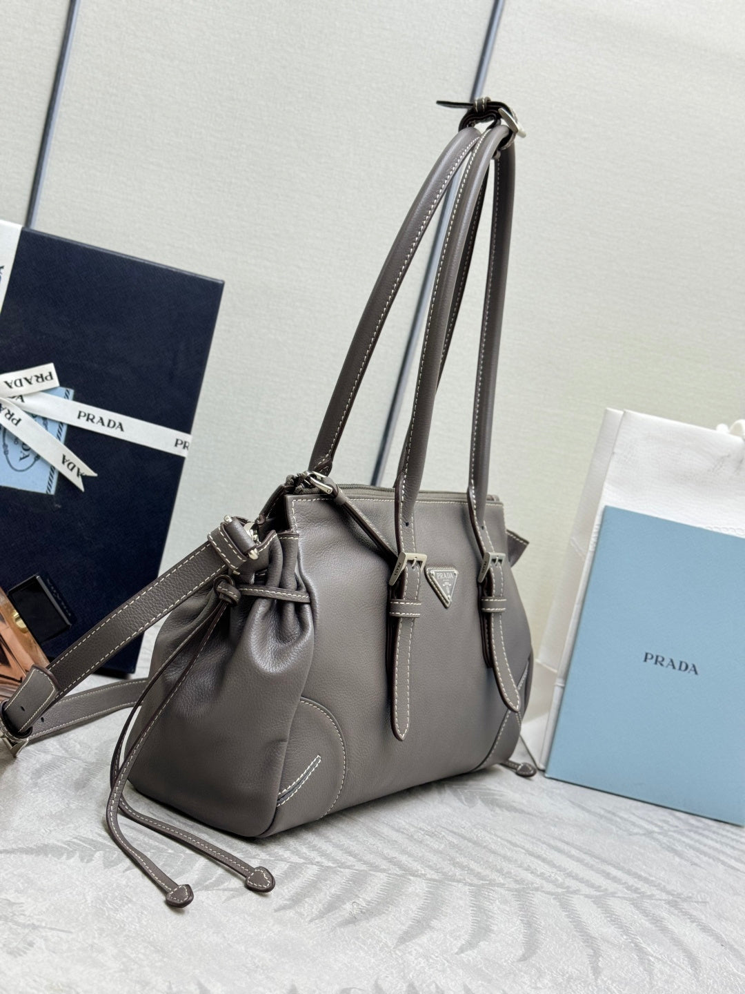 Prada gray leather handbag with adjustable shoulder strap and front logo plate.