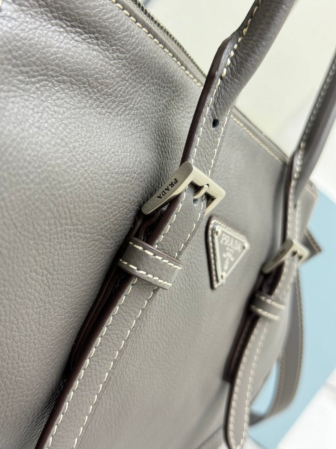 Prada gray leather handbag close-up of stitched pocket and triangle logo plate.