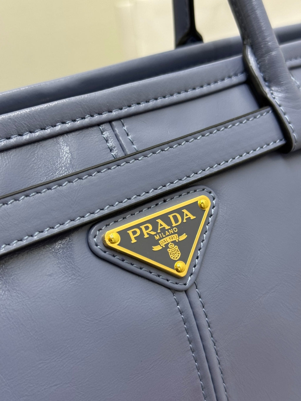Close-up of Prada logo plaque on light blue leather handbag with stitched trim