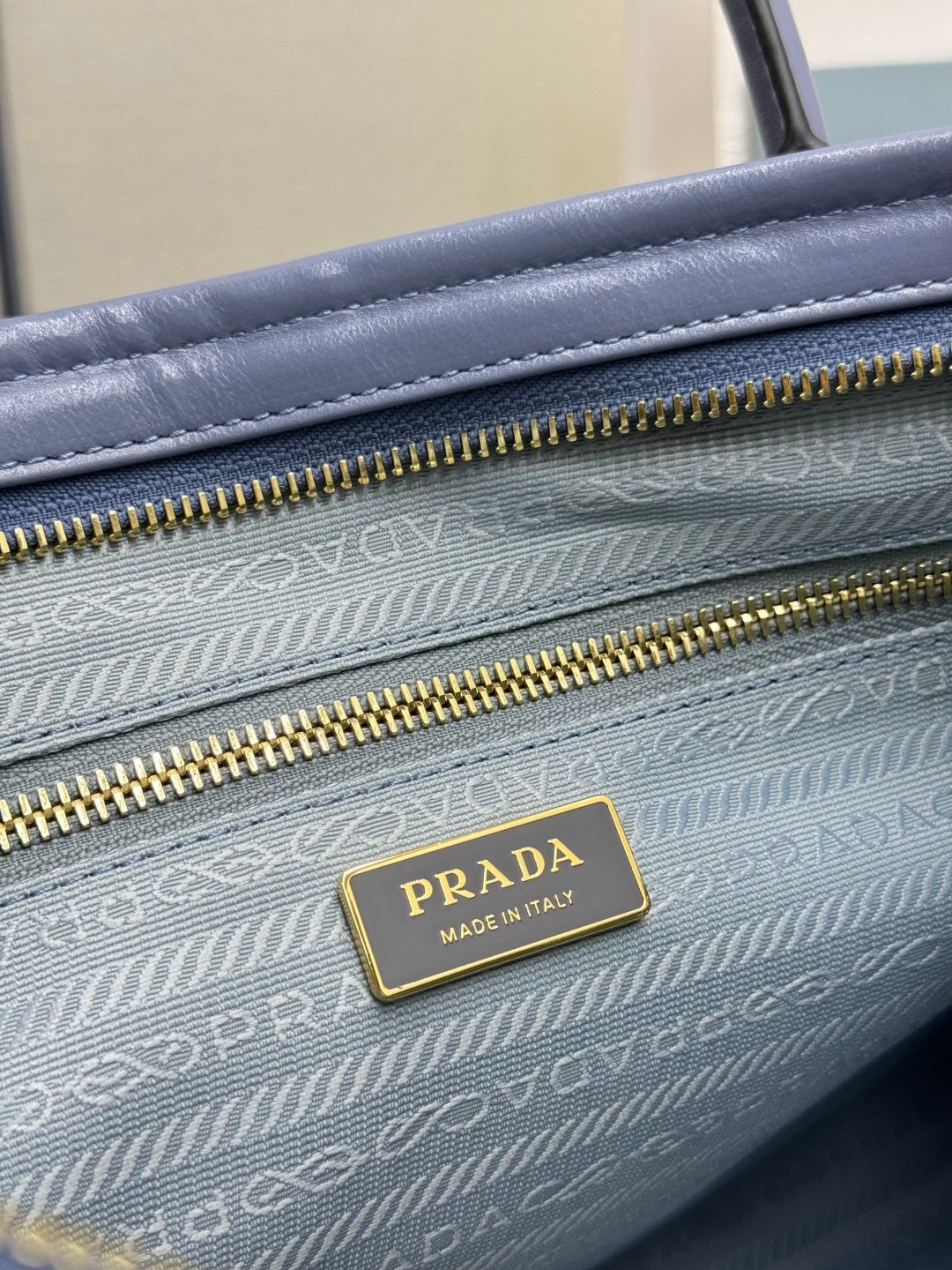 Close-up of Prada lining with zipper track and gold logo plaque inside the bag