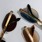 Assorted gold-tone sunglasses with tinted lenses, including dark and blue styles, logo temples