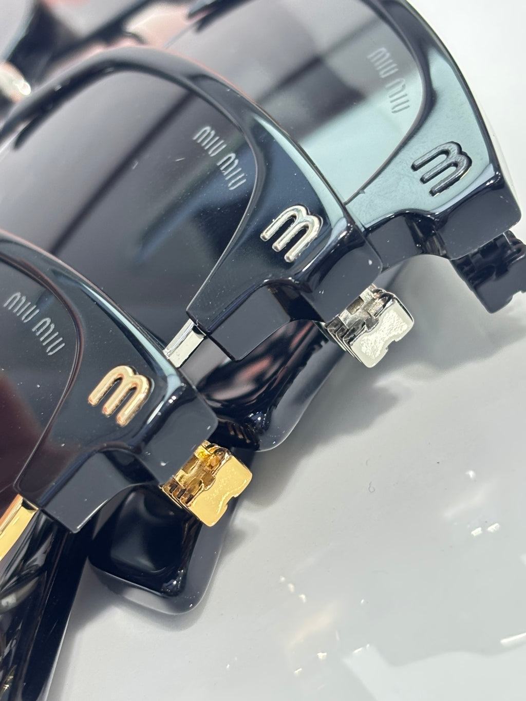 MiuMiu sunglasses close-up with black frames, “miu miu” logo, and gold hinge hardware