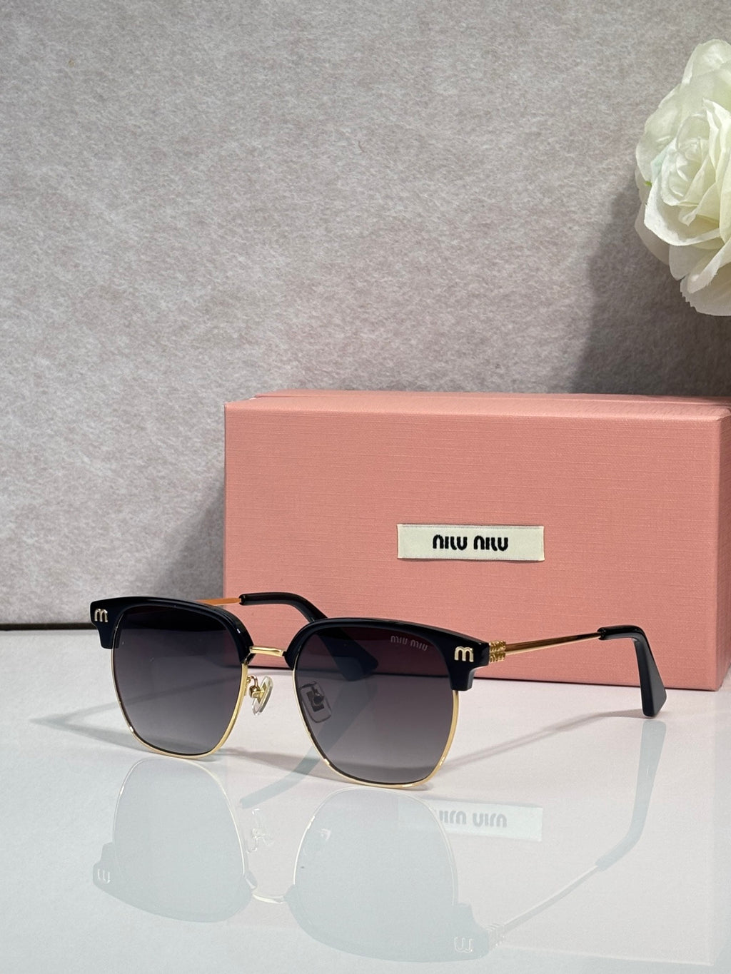 MiuMiu sunglasses with black frames, dark gradient lenses, and gold trim at the bridge