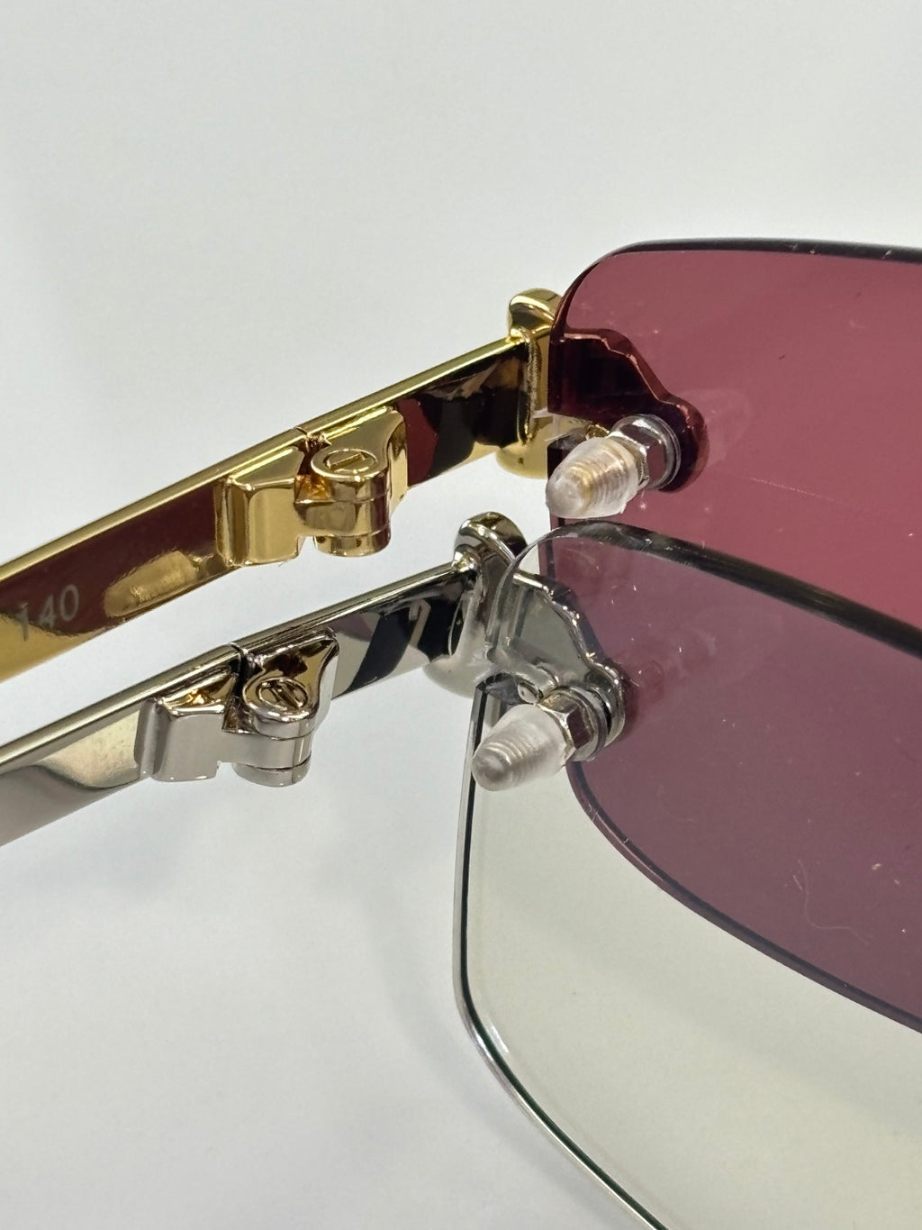 Gold-trim eyeglass hinge with maroon-tinted lens and clear frame hardware